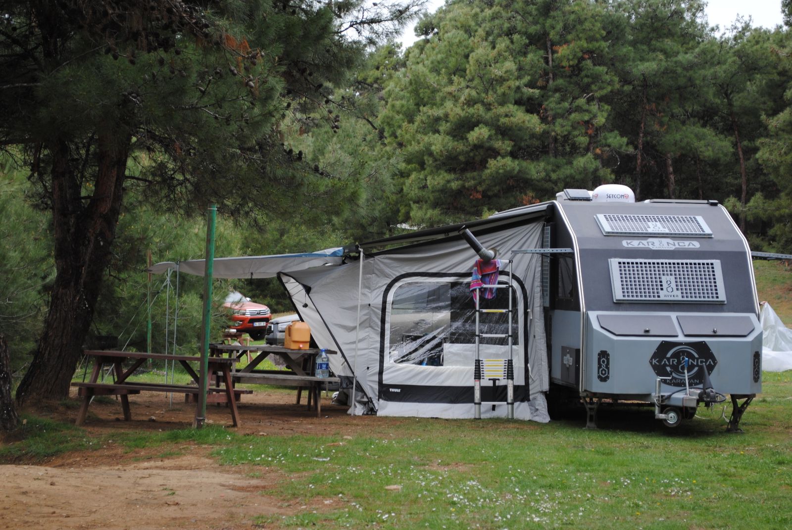 A caravan with an awning at a wooded campsite