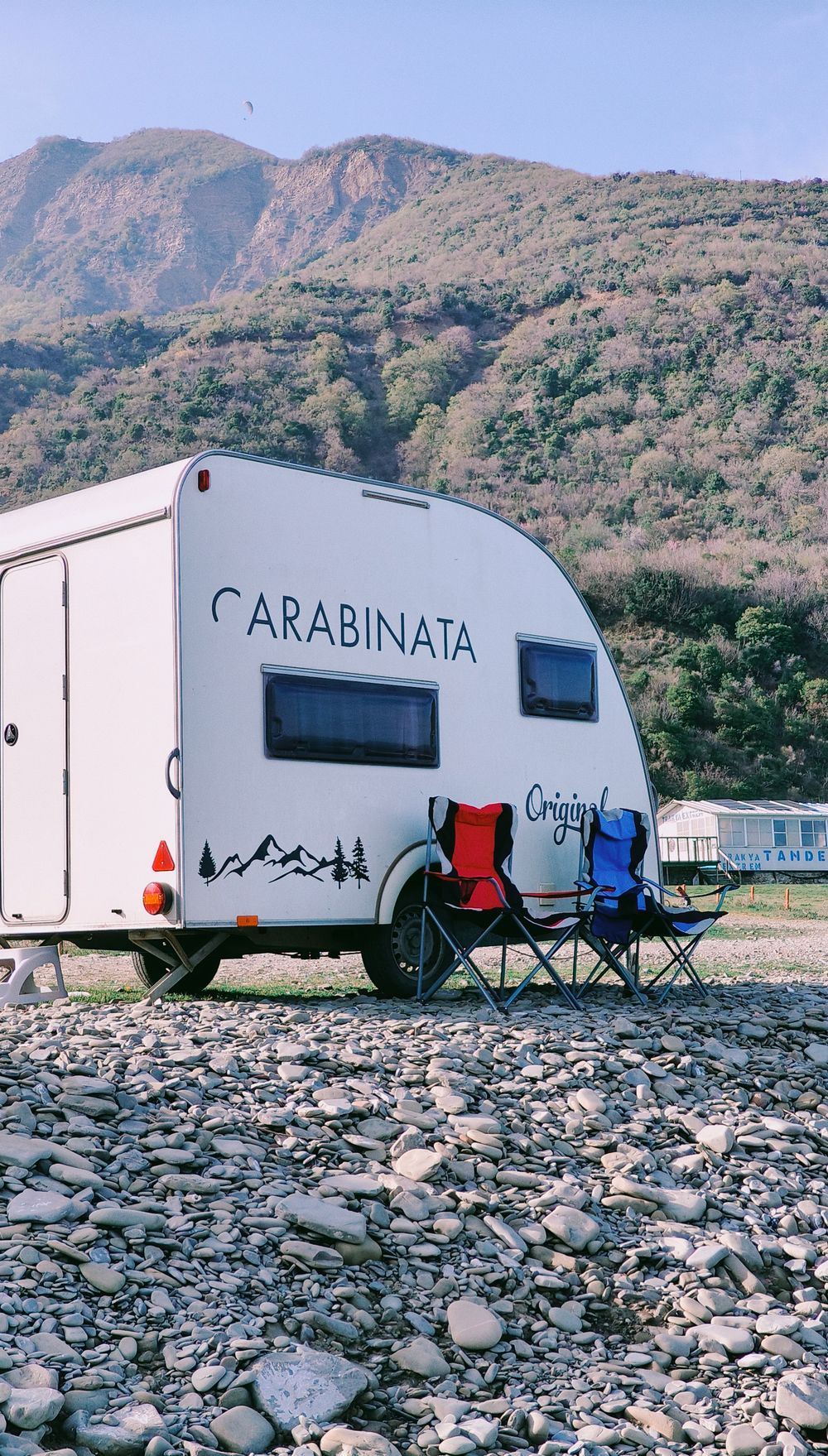 A touring caravan and camping chairs beside mountain scenery